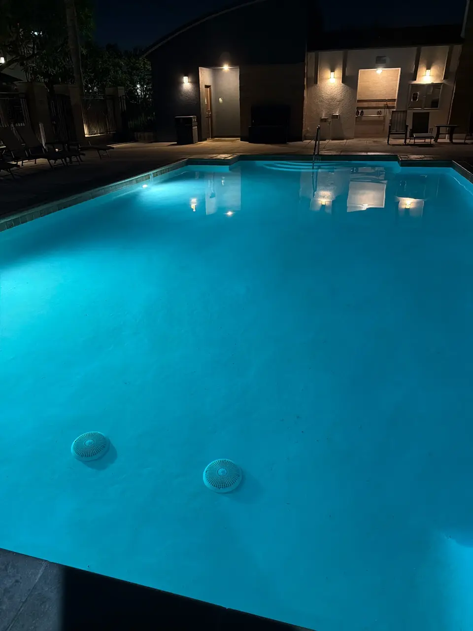 Clear blue pool water glows under underwater lights, with entry steps, a handrail, and surrounding lounge chairs, after pool service in Hawthorne, CA