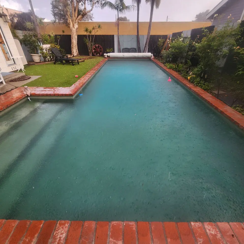Clear turquoise water fills a rectangular pool with wide entry steps, brick coping, and surrounding palms and landscaping, after pool service in Hermosa Beach, CA