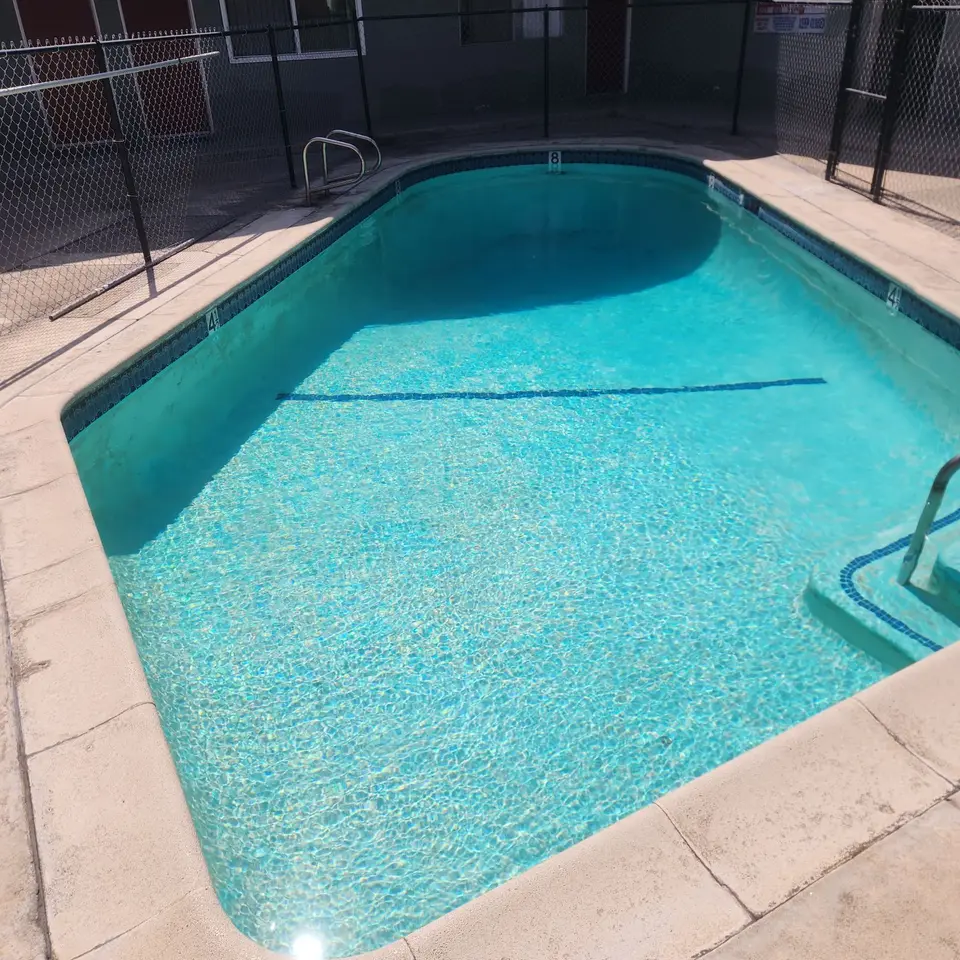 Sparkling turquoise pool water reveals floor markings and entry steps, with blue tile, handrails, and perimeter fencing, after pool service in Inglewood, CA