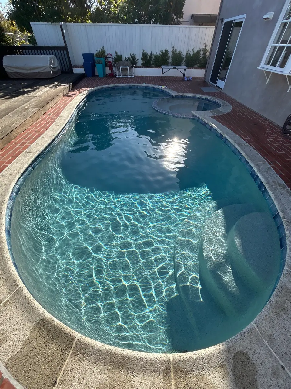 Clear blue water fills a curved pool with entry steps, blue tile, and an attached circular spa, after pool service in La Jolla, CA