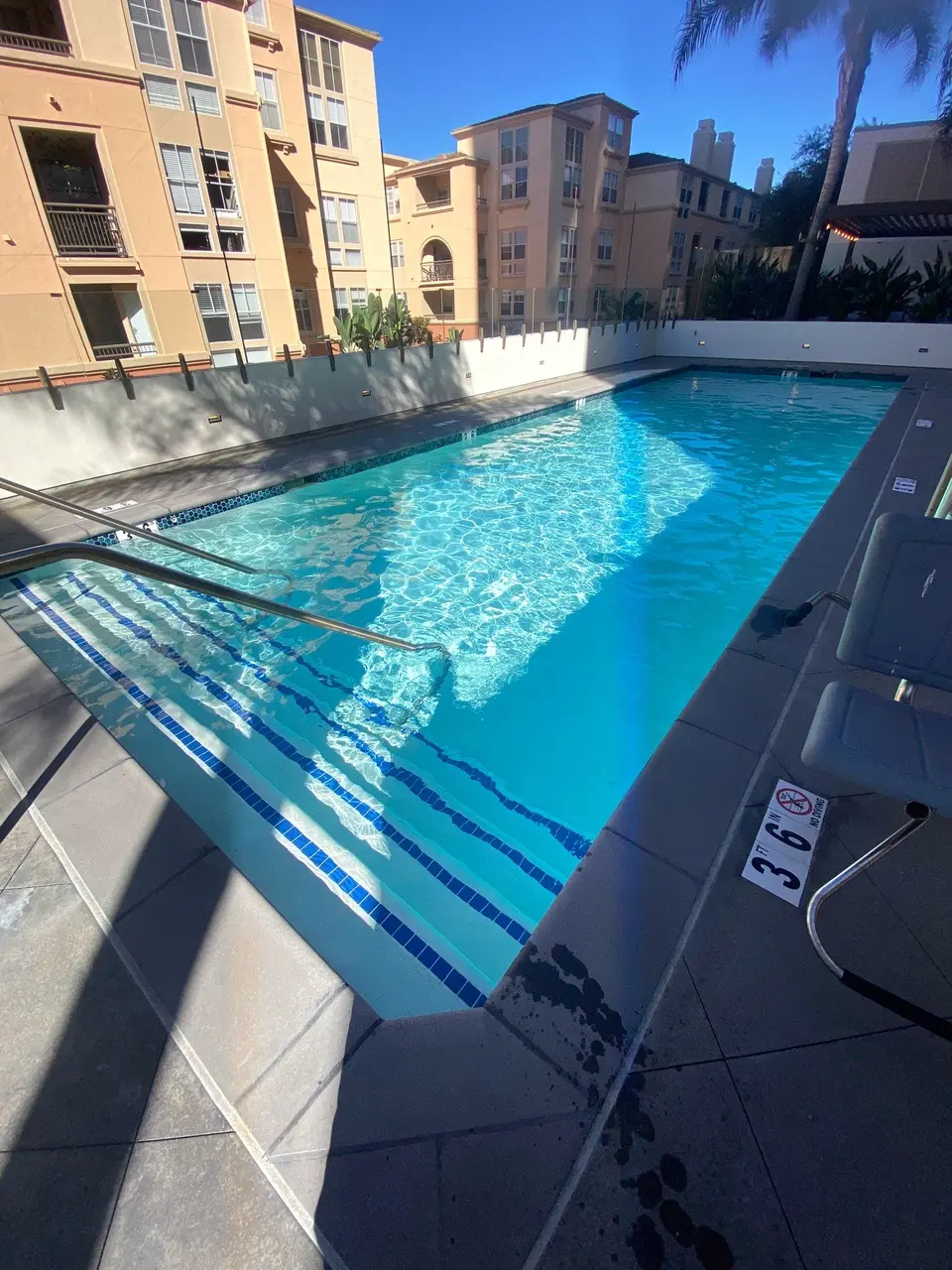 Sparkling blue water fills a rectangular pool with wide tiled entry steps, handrails, and an accessibility lift, after pool service in La Jolla, CA