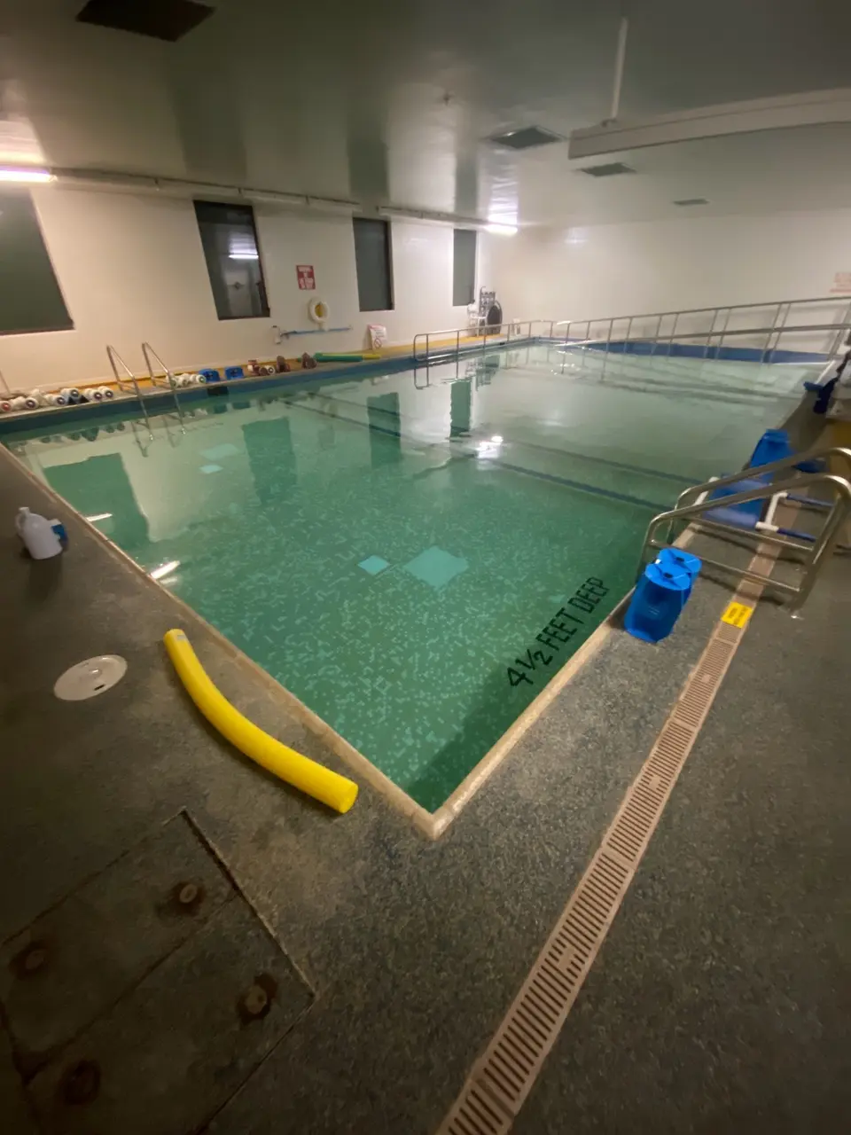 Indoor pool with clear turquoise water, patterned tile, entry ladders, and a railed accessibility ramp, after pool service in La Jolla, CA