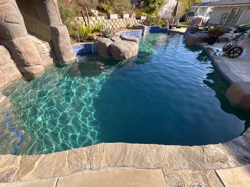 Sparkling blue water fills a freeform pool with a rock grotto, boulder accents, and blue tile, after pool service in Lakeside, CA