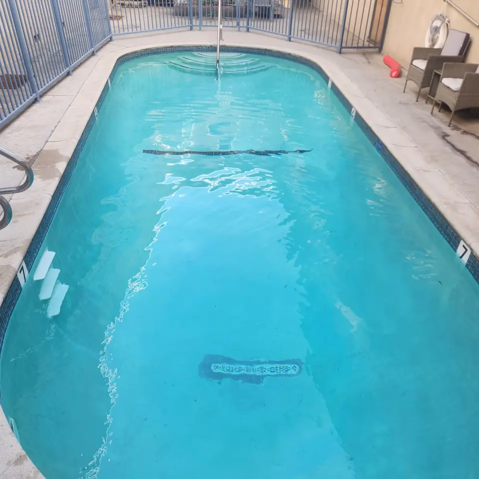 Clear turquoise pool with rounded corners, entry steps, stainless steel handrails, and blue waterline tile, after pool service in Lawndale, CA