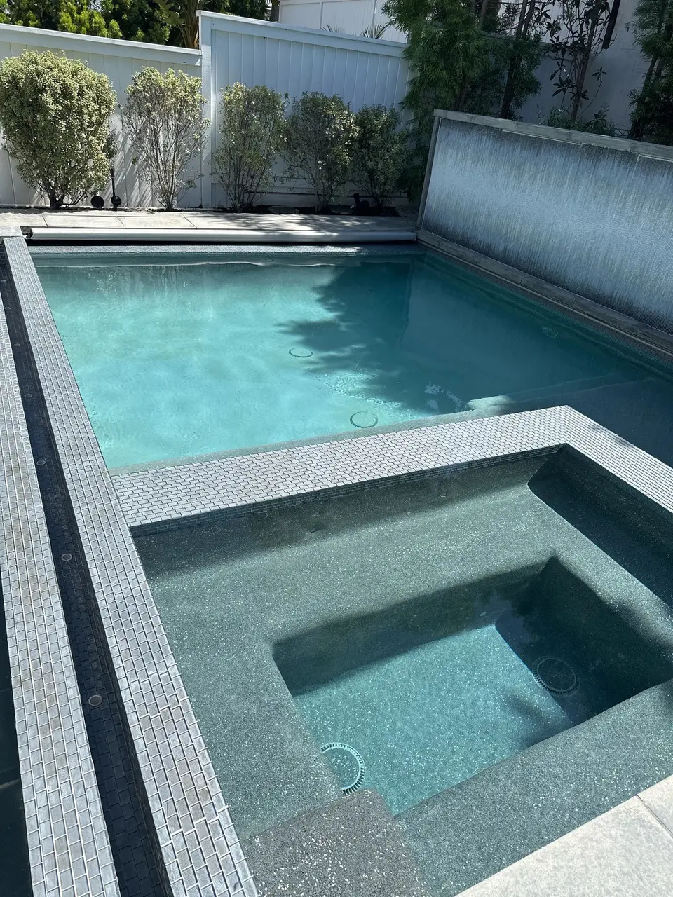 Clear turquoise pool and adjoining spa feature mosaic tile borders, built-in benches, and a wall waterfall, after pool service in Manhattan Beach, CA