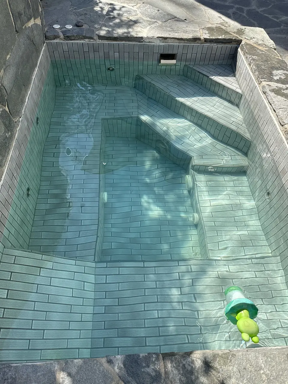 Clear water reveals a tiled spa with built-in steps, benches, jets, and surrounding stone coping, after pool service in Manhattan Beach, CA