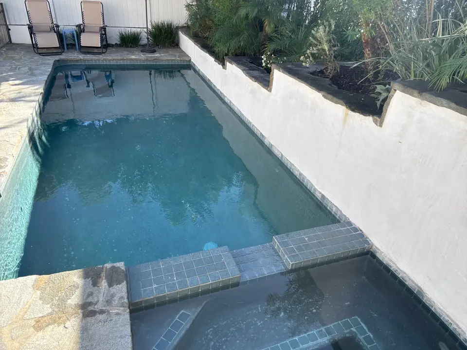 Clear blue water fills a narrow pool with an attached tiled spa beside lush raised landscaping, after pool service in Manhattan Beach, CA