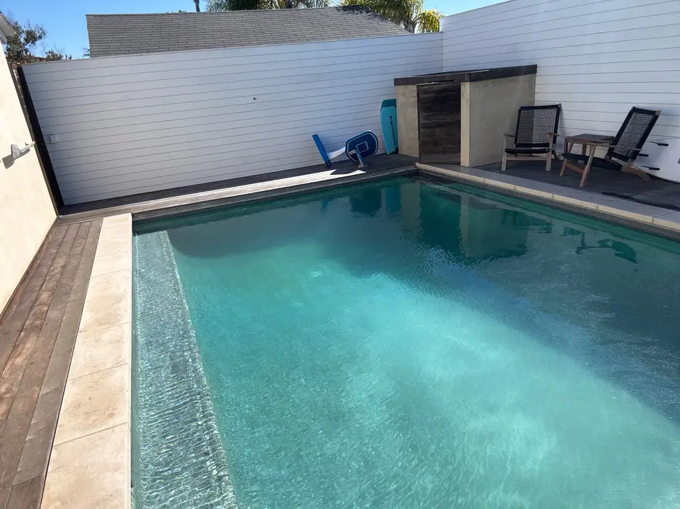 Clear turquoise water fills a rectangular pool with a submerged bench, surrounding decking, and poolside chairs, after pool service in Manhattan Beach, CA