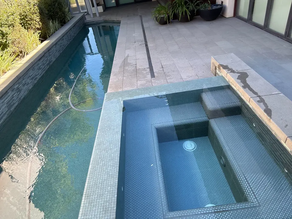 Clear blue water fills a narrow pool and tiled spa with built-in seating beside landscaped borders, after pool service in Manhattan Beach, CA