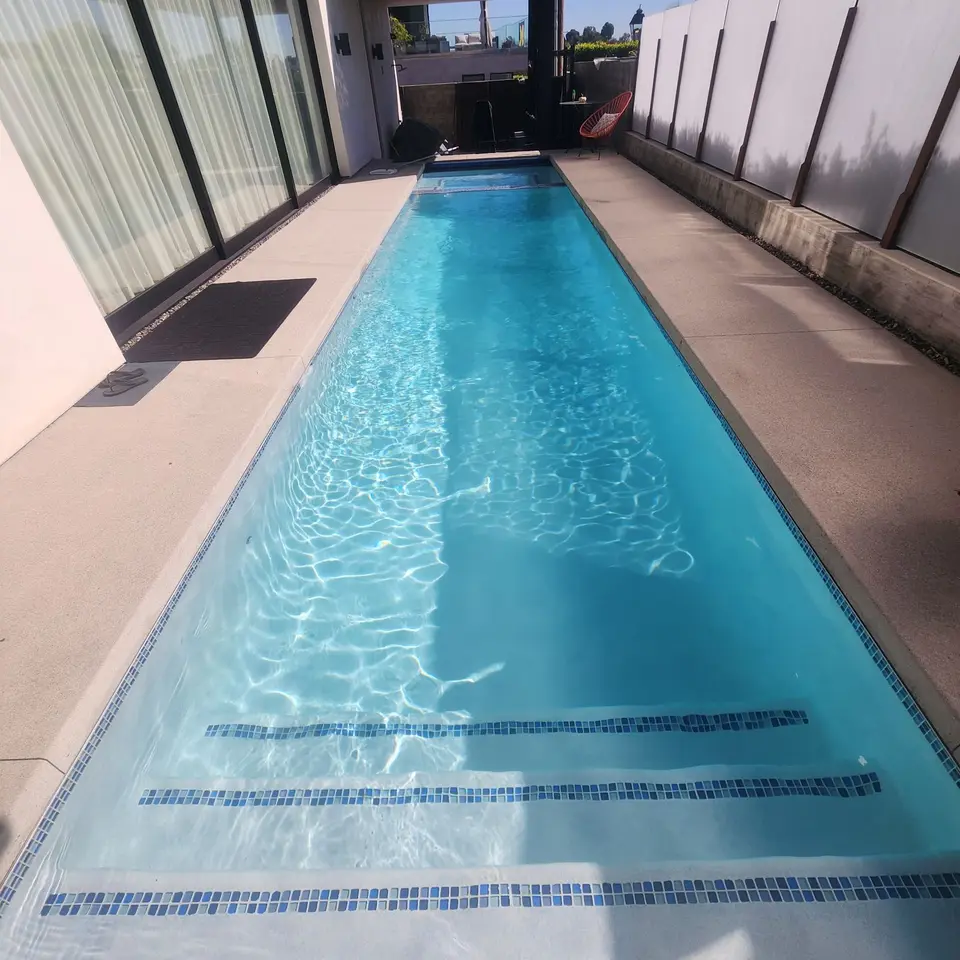 Sparkling blue water fills a narrow lap pool with broad entry steps and blue mosaic tile accents, after pool service in Manhattan Beach, CA