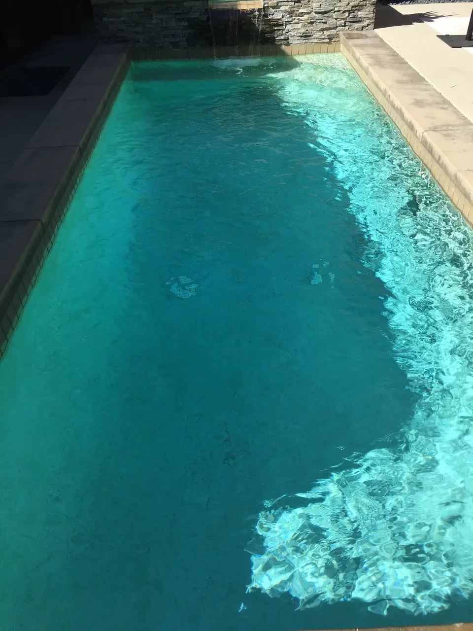 Clear turquoise water fills a rectangular pool with stone coping and a stacked-stone waterfall, after pool service in Manhattan Beach, CA