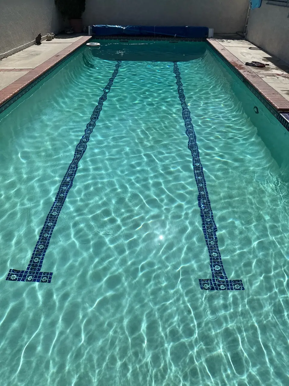 Rectangular pool with sparkling turquoise water, blue tile lane markings, brick coping, and a rolled cover, after pool service in Manhattan Beach, CA