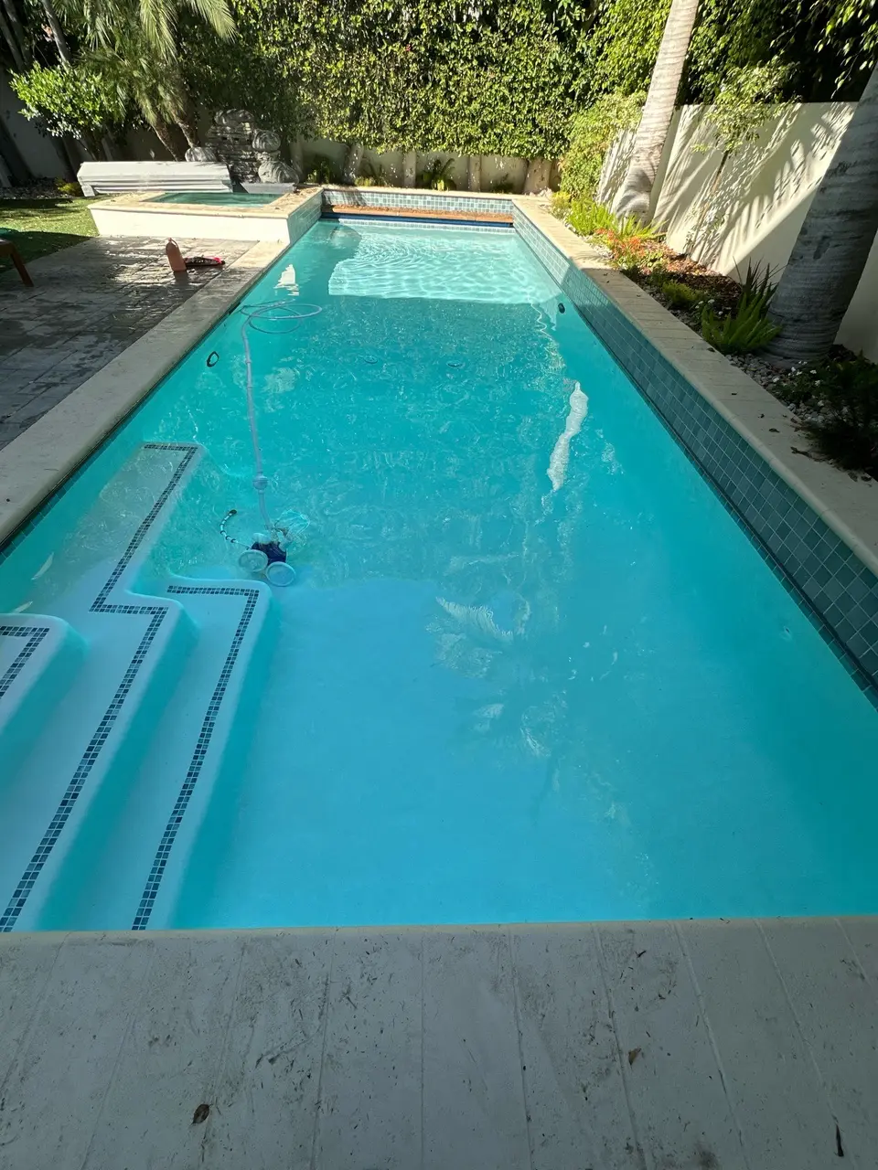 Clear turquoise water fills a rectangular pool with tiled steps, a raised spa, and surrounding palms, after pool service in Manhattan Beach, CA