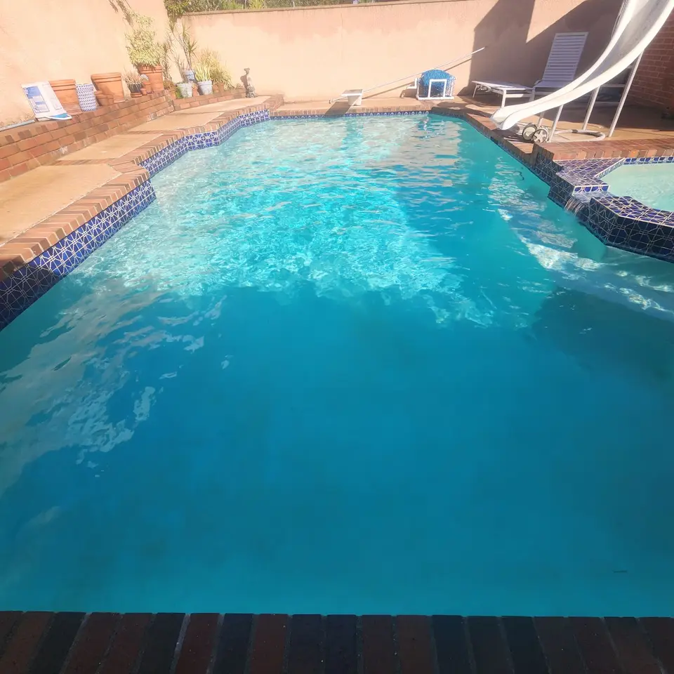 Clear turquoise pool with blue patterned tile, brick coping, attached spa, slide, and diving board, after pool service in Manhattan Beach, CA