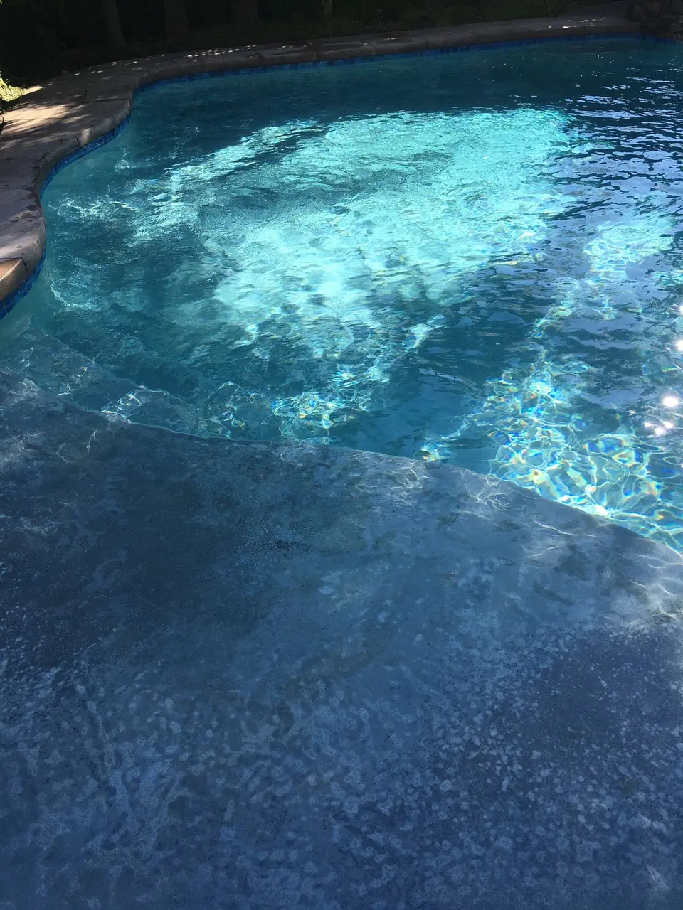 Clear blue pool water ripples over a broad shallow ledge beside curved stone coping and blue waterline tile, after pool service in Manhattan Beach, CA