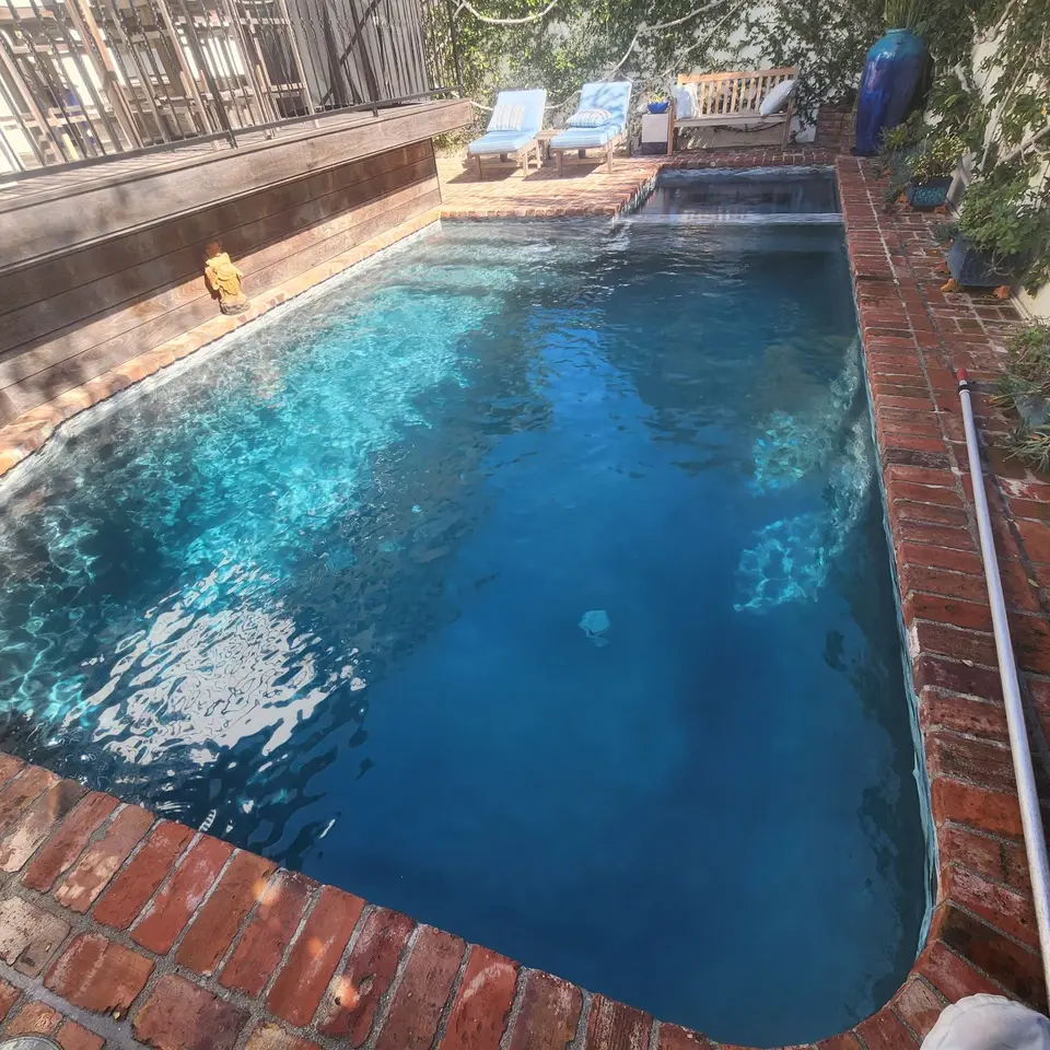 Sparkling blue pool with brick coping, a raised spillover spa, and greenery surrounding a small seating area, after pool service in Manhattan Beach, CA