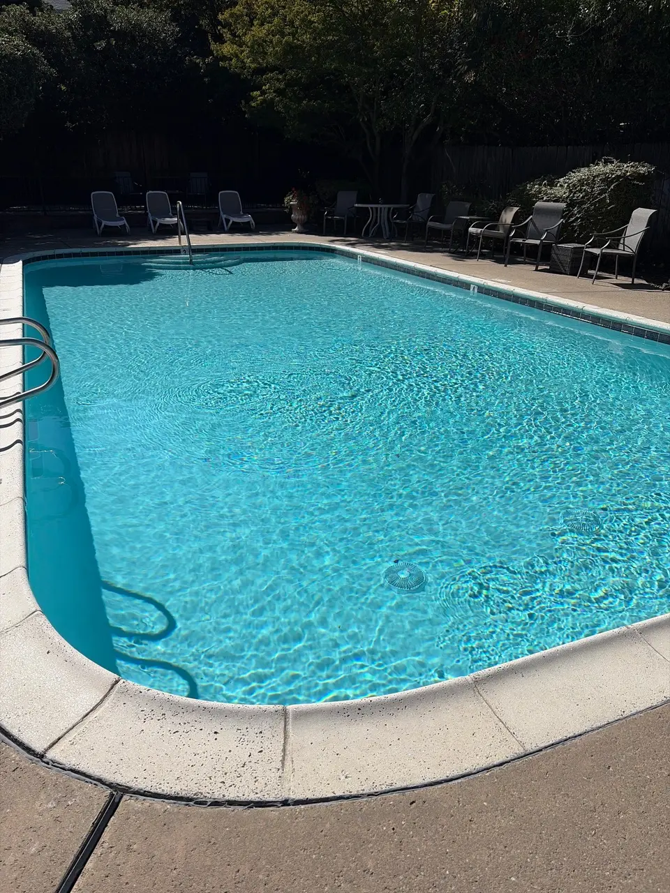 Sparkling turquoise pool water with blue waterline tile, metal handrails, poolside seating, and surrounding trees, after pool service in Orangevale, CA