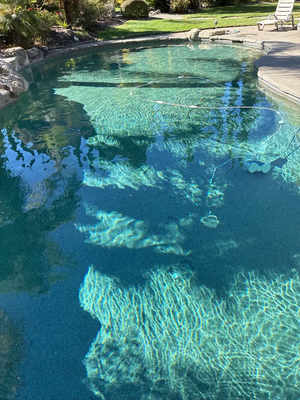 Clear turquoise water reveals textured pool flooring and steps, bordered by rocks, lawn, and landscaping, after pool service in Orangevale, CA