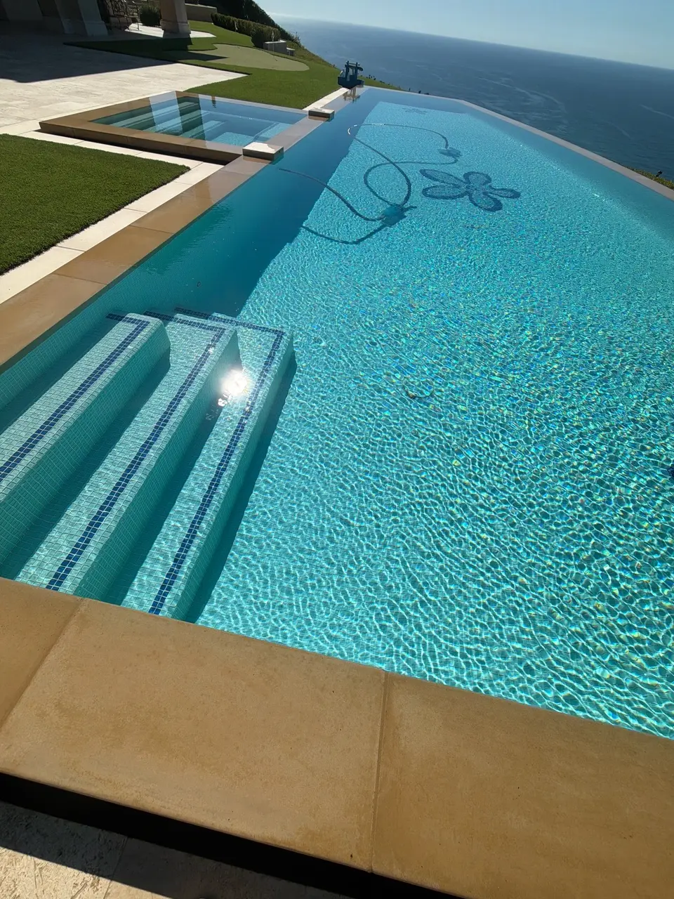Sparkling turquoise water fills a tiled infinity pool with broad entry steps, an attached spa, and ocean views, after pool service in Palos Verdes Estates, CA