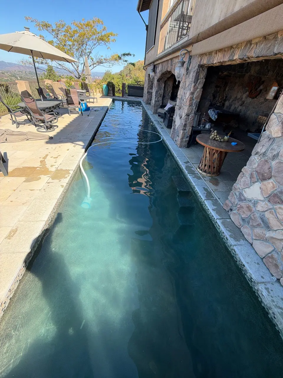 Clear teal water fills a narrow pool beside stone archways, with mosaic edging and poolside loungers, after pool service in Poway, CA