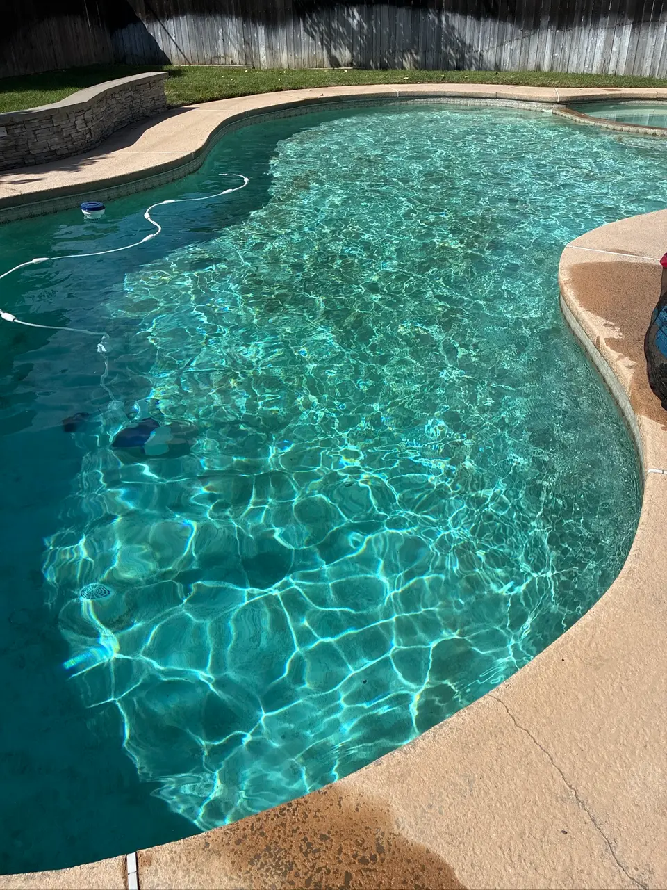 Sparkling turquoise water fills a freeform pool with tan coping, an attached spa, and a submerged cleaner, after pool service in Rancho Cordova, CA
