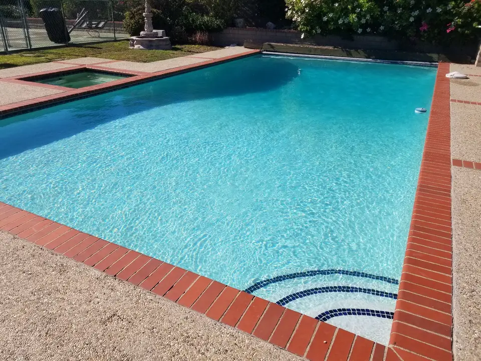 Sparkling turquoise pool with an attached spa, brick coping, curved tiled steps, and flowering landscaping, after pool service in Rancho Palos Verdes, CA