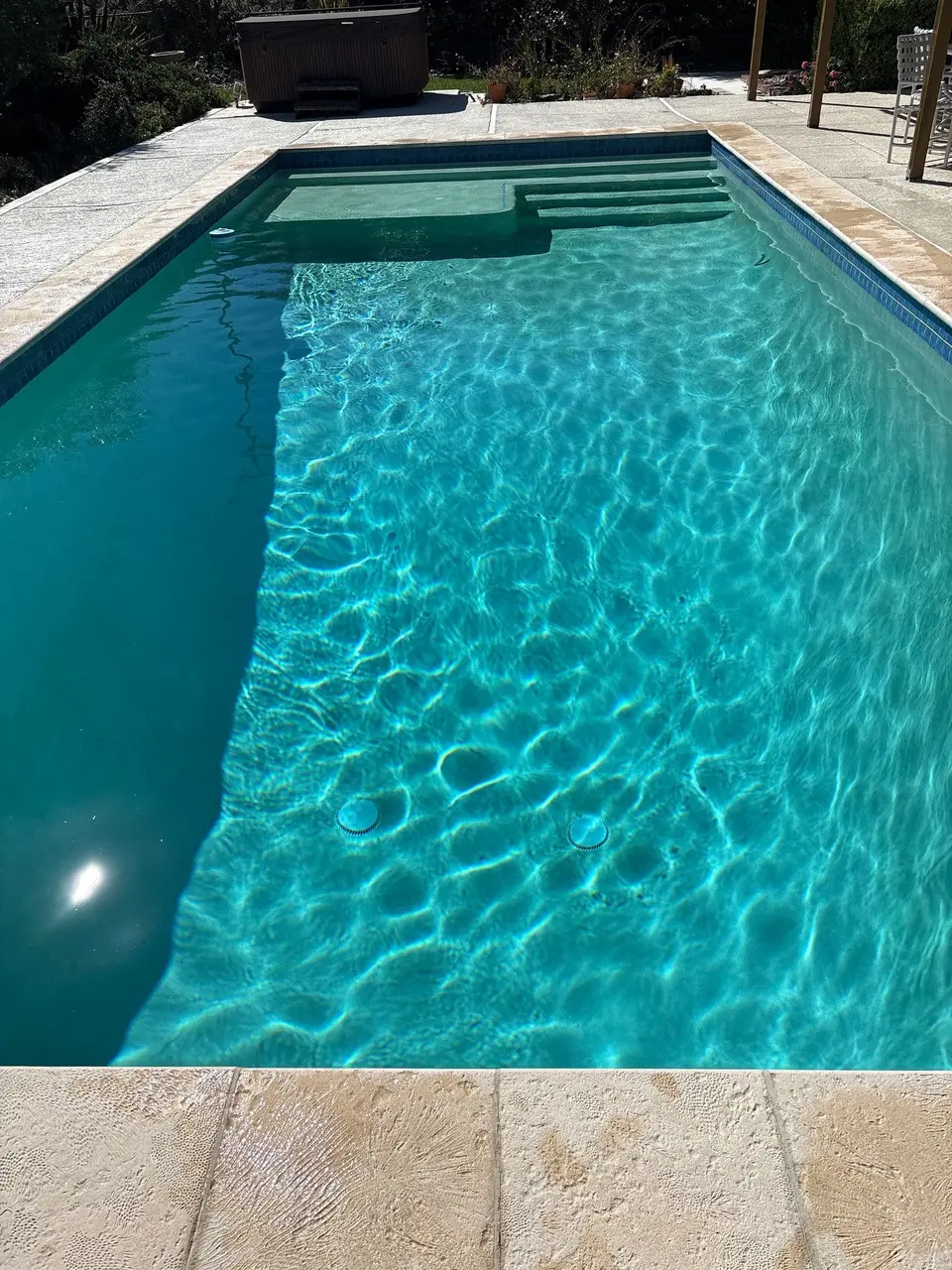 Sparkling turquoise pool water reveals wide entry steps and a submerged bench, bordered by blue tile and stone coping, after pool service in Rancho Palos Verdes, CA