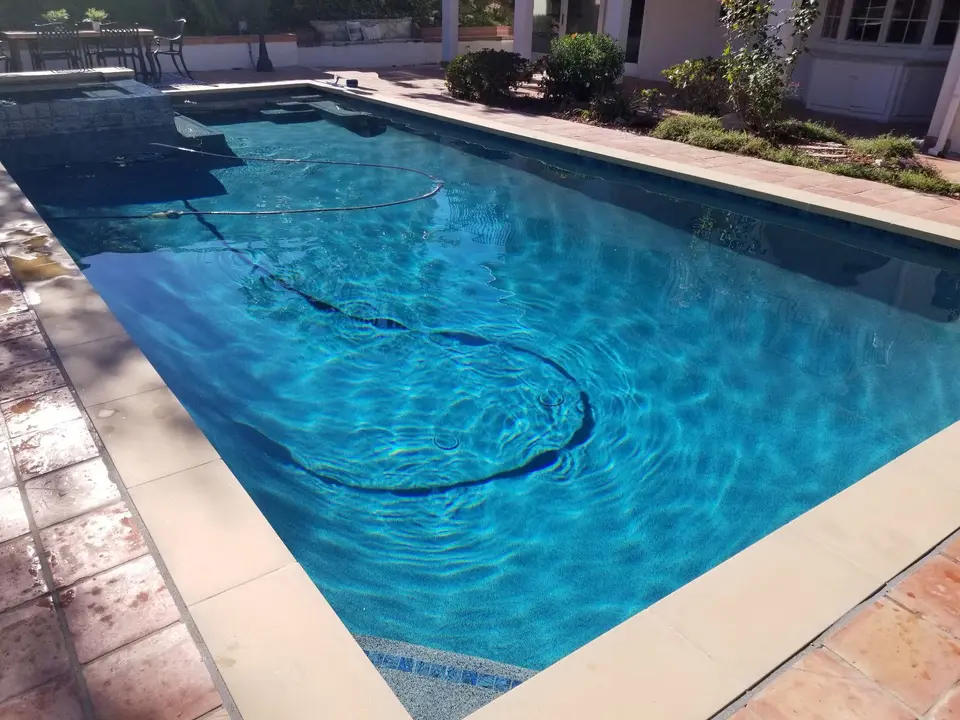 Clear blue pool water surrounds submerged steps beside a raised tiled spa, stone coping, and landscaped borders, after pool service in Rancho Palos Verdes, CA