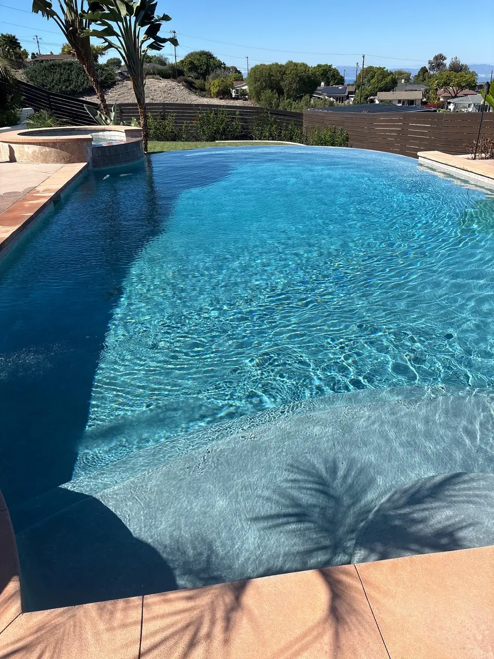 Sparkling blue pool with a wide shallow entry, raised spa, infinity edge, and tropical landscaping, after pool service in Rancho Palos Verdes, CA