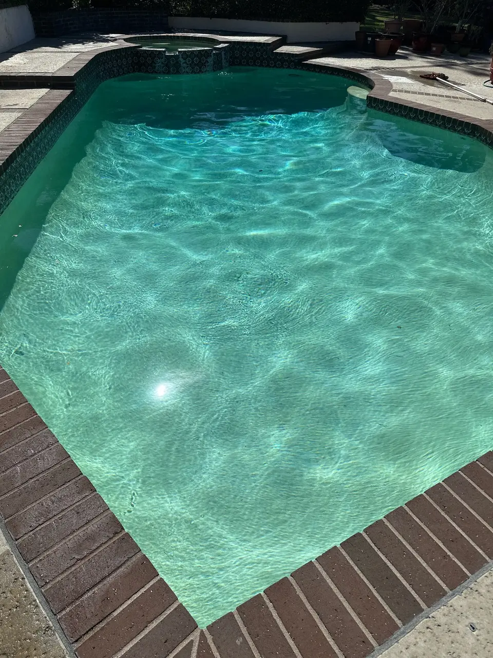 Clear turquoise water fills a curved pool with brick coping, patterned tile, a raised spa, and underwater seating, after pool service in Rancho Palos Verdes, CA