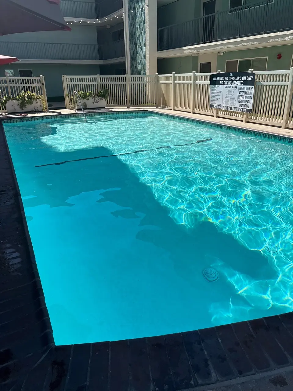 Sparkling turquoise water fills a rectangular courtyard pool bordered by dark tile, brick coping, and white fencing, after pool service in Rancho Palos Verdes, CA