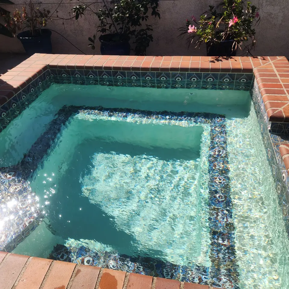Spa with sparkling turquoise water, decorative patterned tile, submerged seating, brick coping, and surrounding potted plants, after pool service in Rancho Palos Verdes, CA