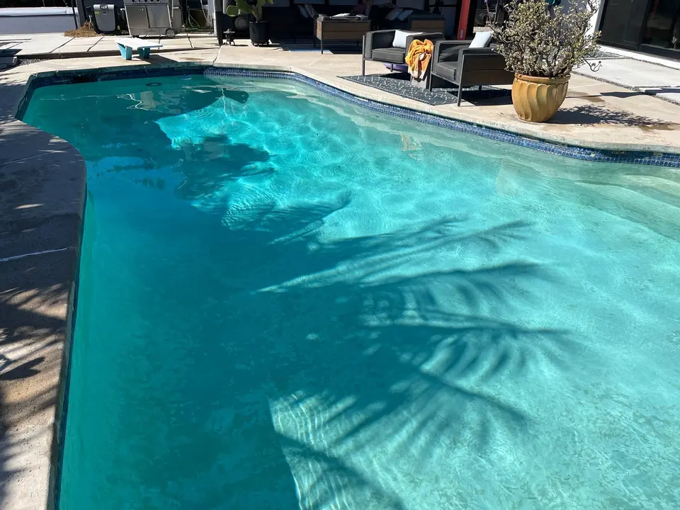 Sparkling turquoise water fills a freeform pool with blue waterline tile, submerged steps, and surrounding patio seating, after pool service in Rancho Palos Verdes, CA
