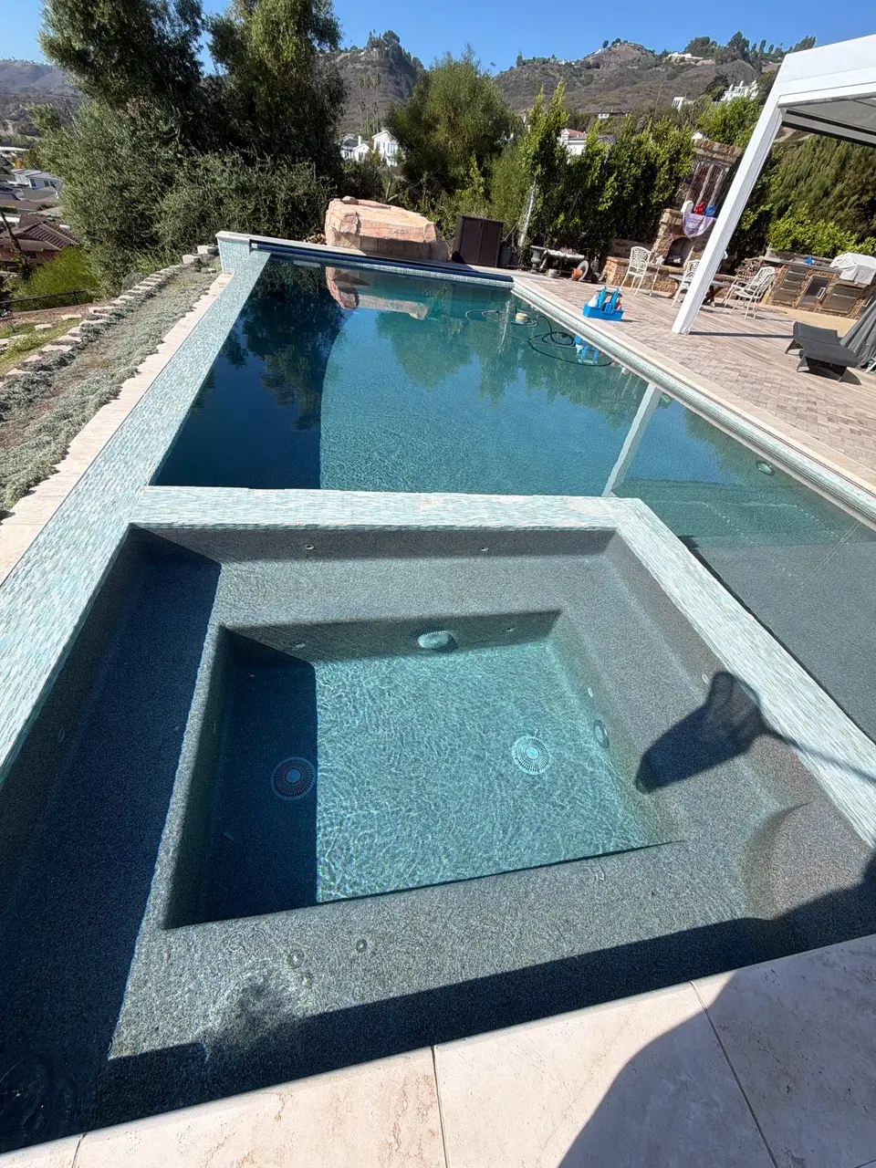 Clear blue water fills a rectangular pool and attached tiled spa beside a landscaped patio, after pool service in Rancho Palos Verdes, CA