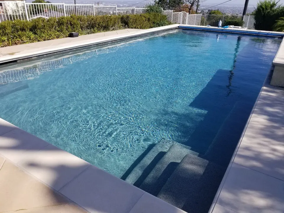 Sparkling blue water fills a rectangular pool with submerged entry steps, light stone coping, and surrounding hedges, after pool service in Rancho Palos Verdes, CA