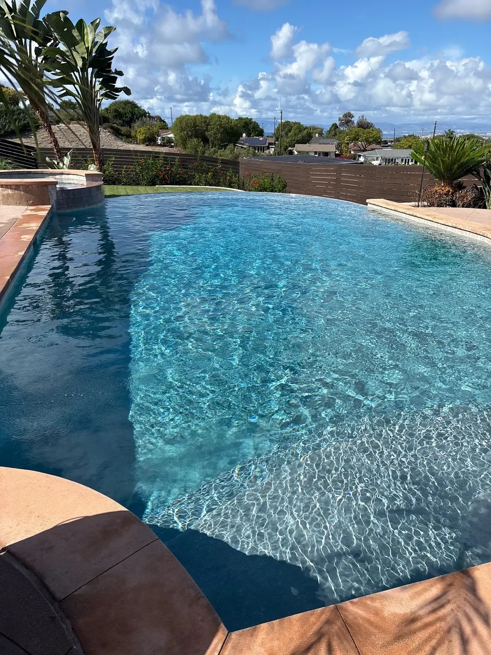 Sparkling blue pool with submerged entry steps, a raised spa, stone coping, and tropical landscaping, after pool service in Rancho Palos Verdes, CA