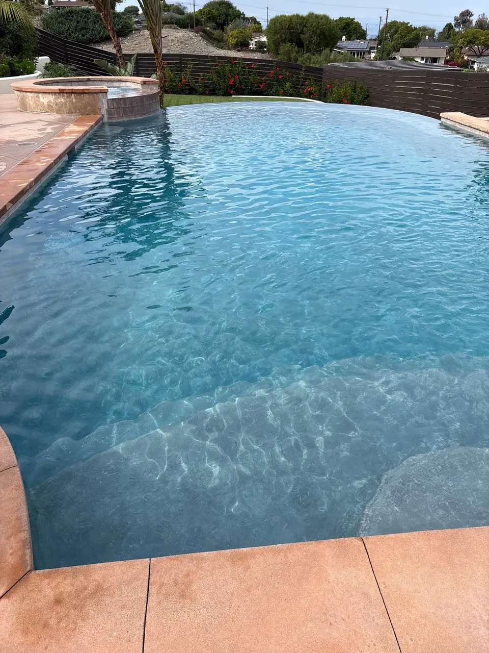 Sparkling blue pool water reveals entry steps beneath a raised circular spa, with palms and flowering landscaping, after pool service in Rancho Palos Verdes, CA