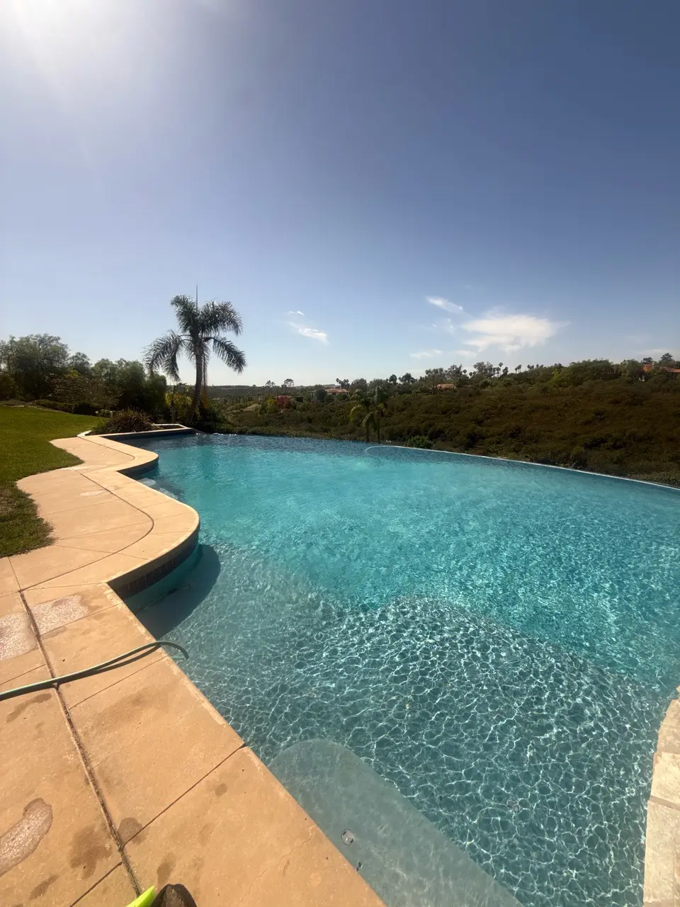 Sparkling turquoise water fills an infinity-edge pool with submerged steps, curved stone coping, and hillside landscaping, after callback in Rancho Santa Fe, CA