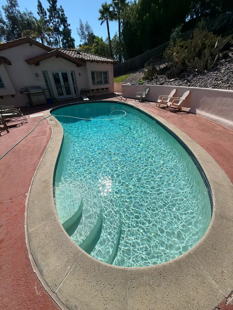 Sparkling turquoise water fills a freeform pool with curved entry steps, surrounded by red decking and cactus landscaping, after pool service in Rancho Santa Fe, CA