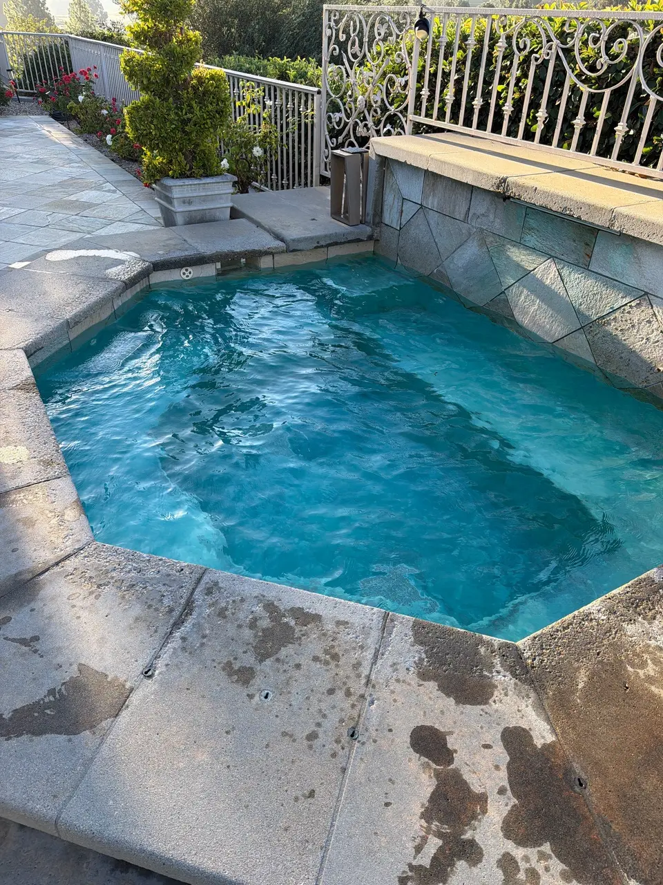 Clear turquoise spa water swirls beneath active jets, surrounded by stone coping, a raised wall, and landscaping, after pool service in Rancho Santa Fe, CA