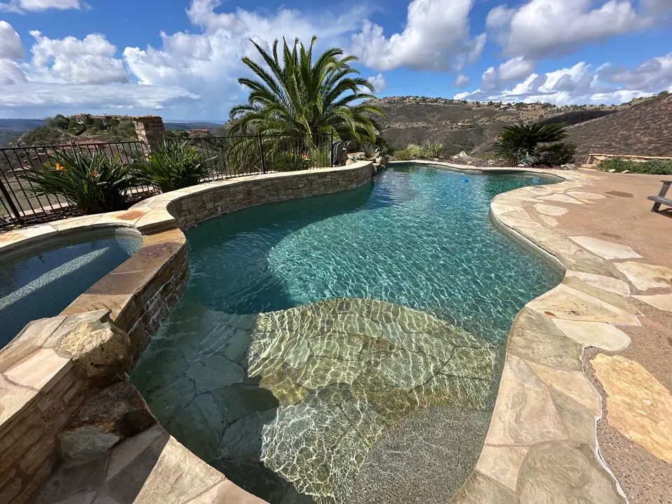 Sparkling turquoise pool with shallow entry steps, an attached raised spa, stone coping, and palm landscaping, after pool service in Rancho Santa Fe, CA