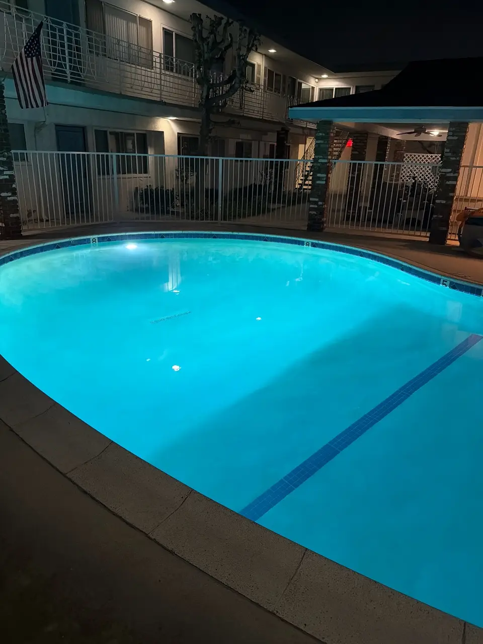 Clear turquoise pool water glows under underwater lighting, with blue tile accents and a surrounding courtyard fence, after pool service in Redondo Beach, CA