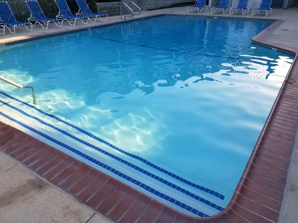 Clear blue pool water surrounds blue-tiled entry steps, with metal handrails, brick coping, and poolside lounge chairs, after pool service in Redondo Beach, CA