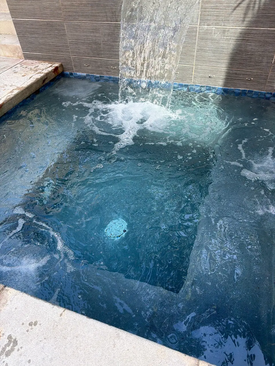 Clear blue spa water with submerged seating, blue tile, stone coping, and a sheet waterfall, after pool service in Redondo Beach, CA