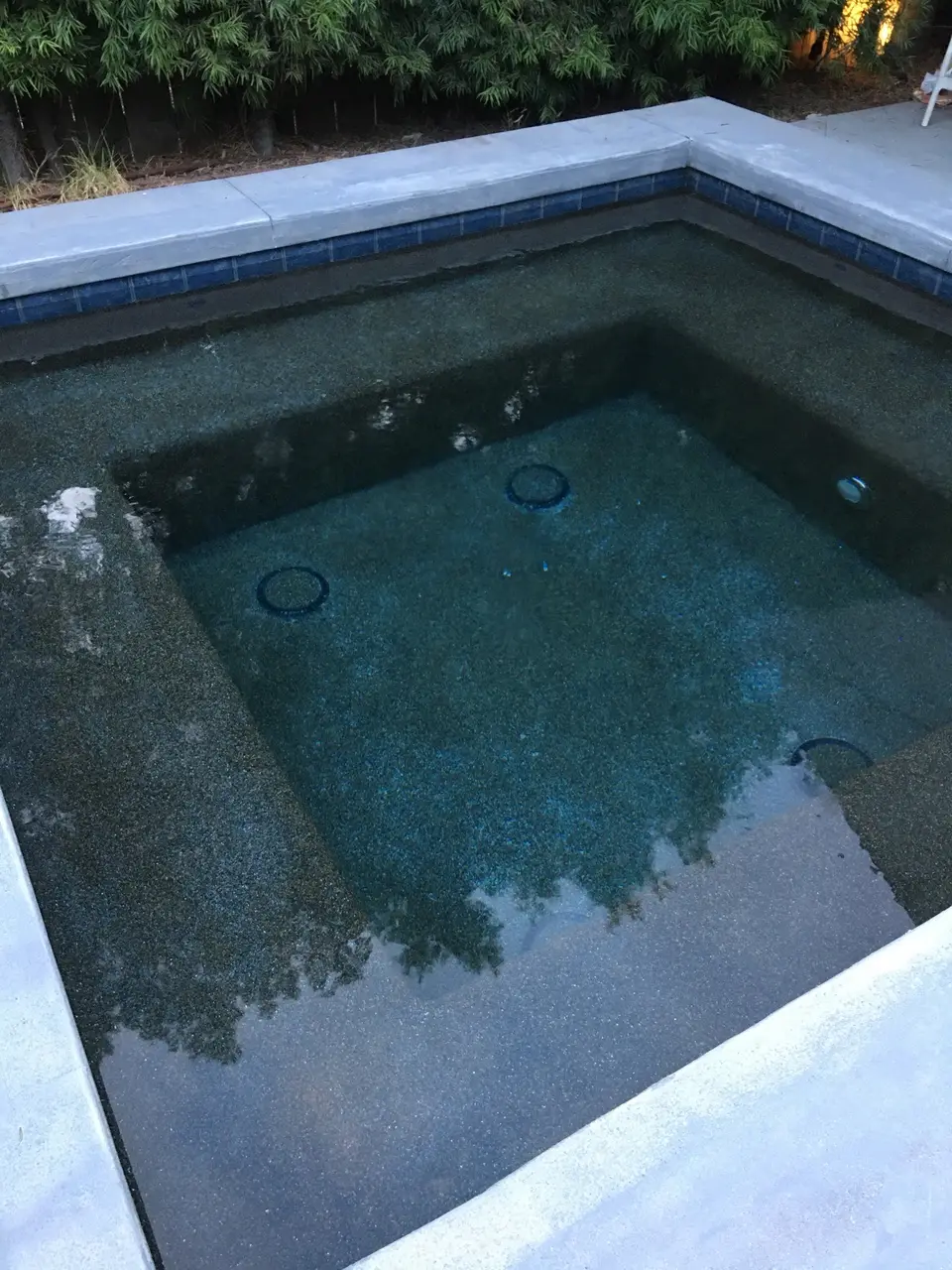 Clear water fills a square spa with dark aggregate finish, bench seating, blue tile, and light stone coping, after pool service in Redondo Beach, CA