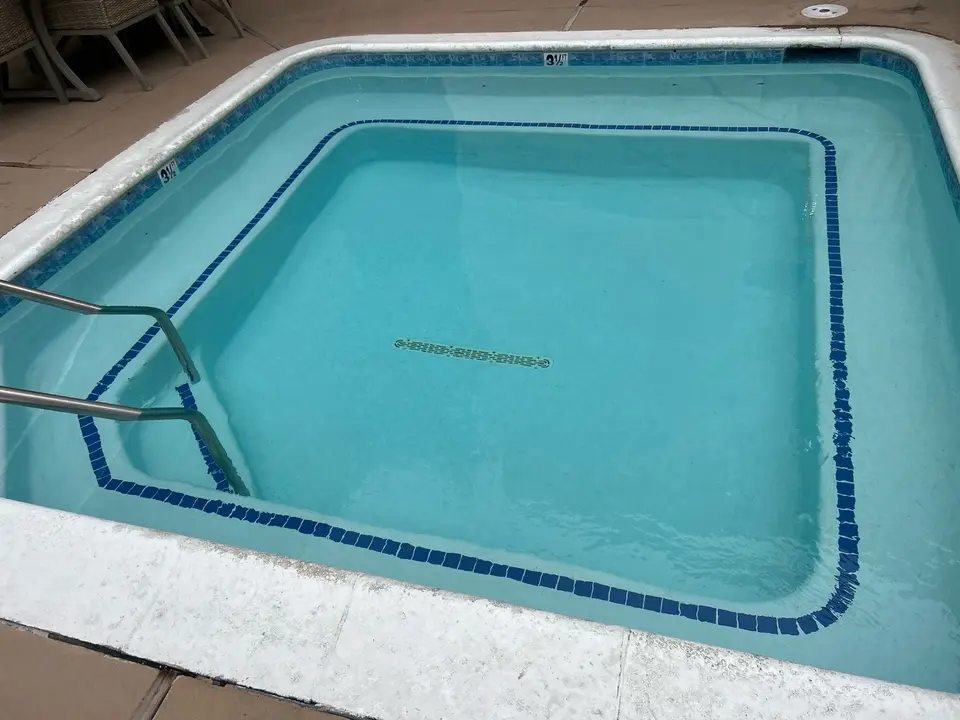 Rectangular spa with clear turquoise water, perimeter bench seating, blue tile trim, and stainless steel handrails, after pool service in Redondo Beach, CA