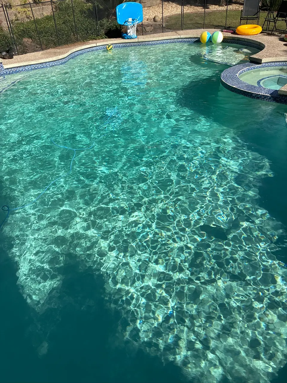 Sparkling turquoise pool water surrounds a raised blue-tiled spa, with beach balls and a poolside basketball hoop, after pool service in Rocklin, CA