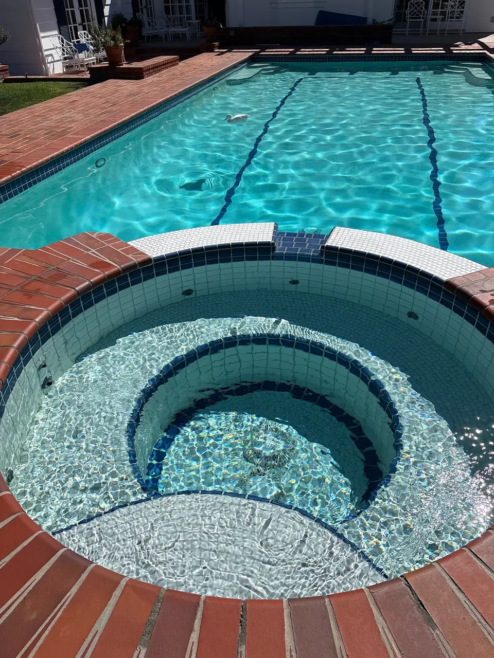 Sparkling turquoise pool with blue lane markings and an attached circular tiled spa surrounded by brick coping, after pool service in Rolling Hills Estates, CA