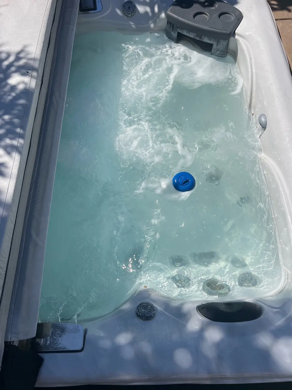 Clear pale blue spa water bubbles over molded seating and jets, with a floating chemical dispenser, after pool service in Roseville, CA