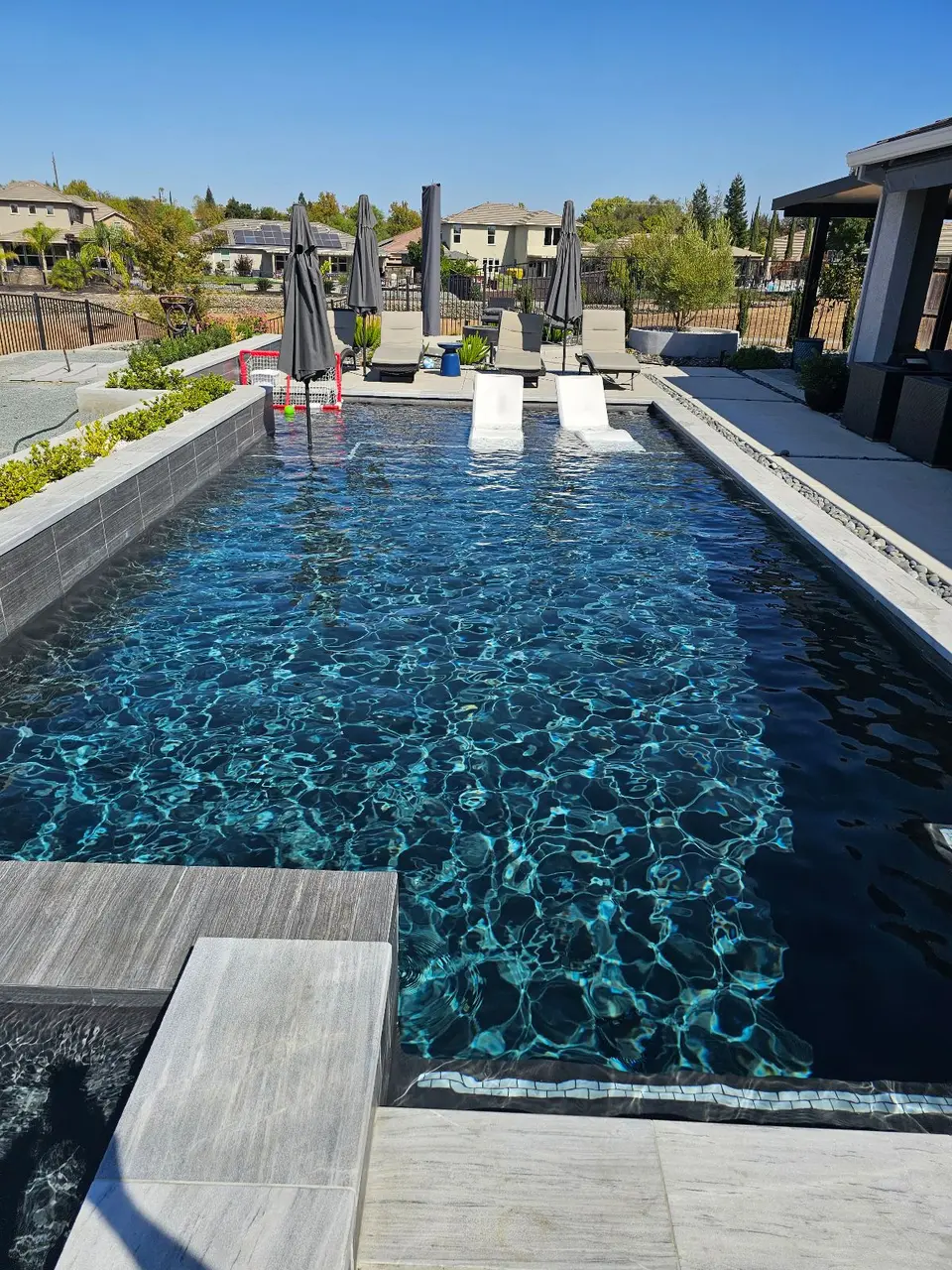 Sparkling dark blue pool with submerged loungers, an attached spa, gray tile, and landscaped planters, after pool service in Roseville, CA